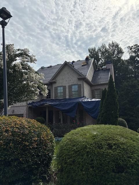 Tarps protecting the porch and landscaping while the storm-damaged roof above is torn off